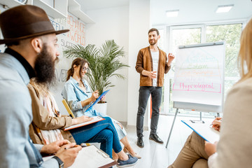 Group of diverse people during the psychological seminar with male coach showing on flipchart in the office