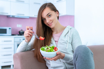 Wall Mural - Portrait of young happy healthy woman eating vegetable salad for lunch at home. Diet and fitness eating. Clean and control food