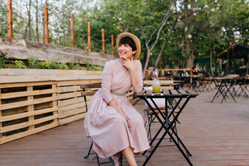 excited brunette girl in beautiful old-fashioned dress touching face with charming smile resting in 