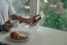 Hands Of Unrecognisable Man Holding Cup Of Coffee And Reading On Tablet In The Morning.
