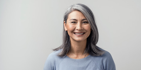 beautiful asian with grey hair smiling standing near the wall