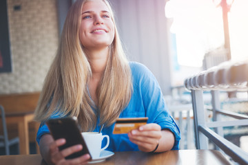 Beautiful young blonde girl in a cafe with a credit card in her hands. Online payment, digital banking shopping concept.