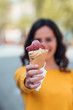 © bnenin - Young woman holding ice cream cone toward camera, focus on the foreground.