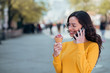 © bnenin - Young woman in the city on a sunny day, eating ice cream and talking on smart phone, copy space.