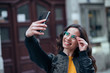 © bnenin - Casual smiling woman taking selfie on smart phone in the town street, close-up.