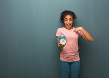 Young Black Woman Surprised, Feels Successful And Prosperous. She Is Holding An Alarm Clock.