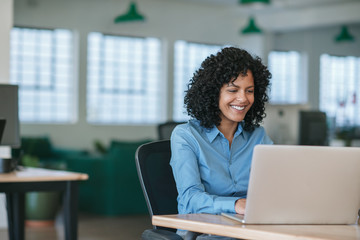 Smiling young businesswoman working on a laptop at her desk