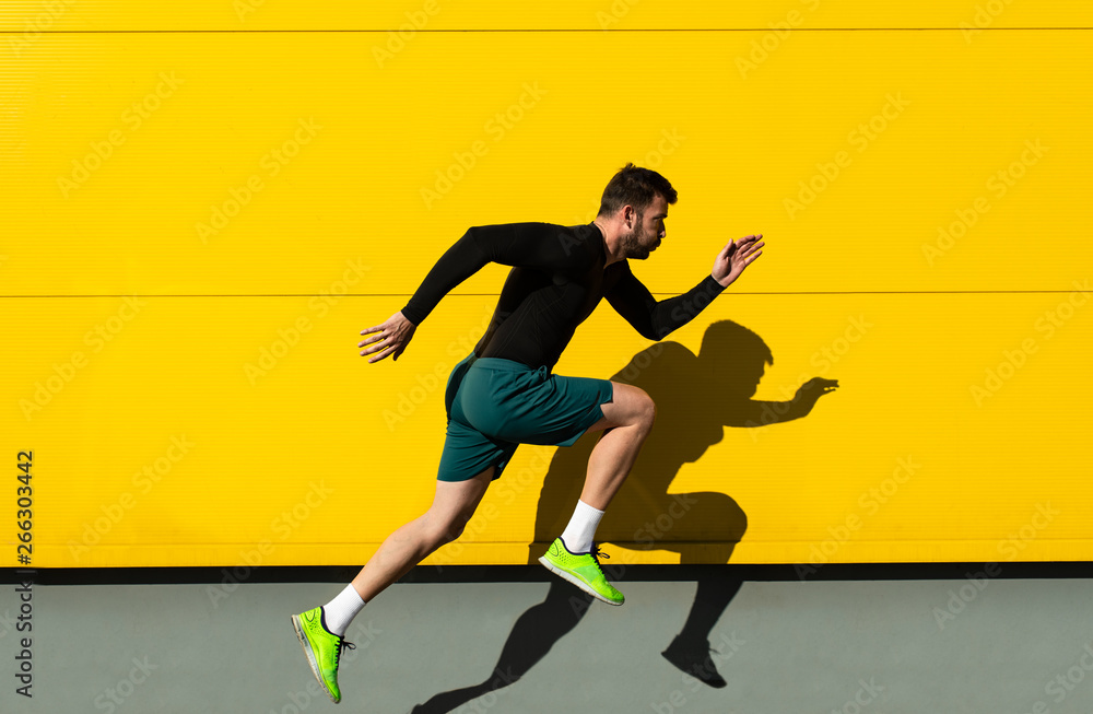 Portrait of male athlete running isolated on yellow wall. - obrazy, fototapety, plakaty 