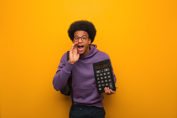 Young african american student man holding a calculator shouting something happy to the front