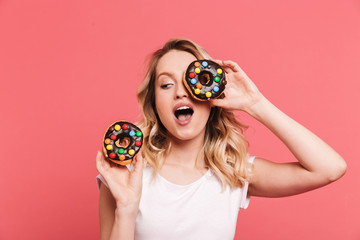 Sticker - Portrait of joyous blond woman 20s wearing casual t-shirt smiling while holding tasty sweet donuts