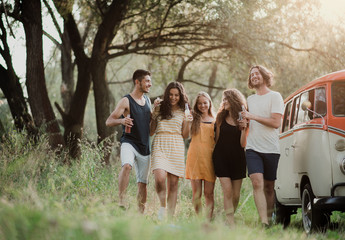 A group of young friends on a roadtrip through countryside, holding bottles and walking.