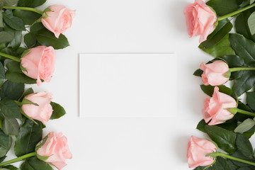 Top view of a white card mockup with pink roses on a white table.