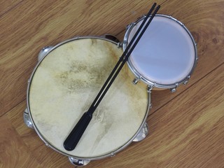 Close-up of two Brazilian percussion musical instruments: pandeiro (tambourine) and tamborim with drumstick on a wooden surface. The instruments are widely used to accompany samba music.