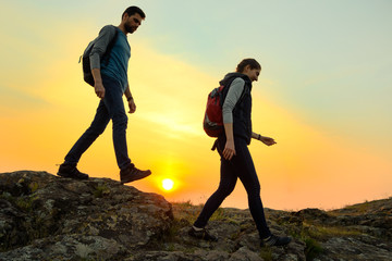 Wall Mural - young happy travelers hiking with backpacks on the rocky trail at summer sunset. family travel and a