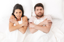 Displeased Frozen Young Loving Couple Lies In Bed Hide Under Blanket.