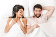 Happy excited young loving couple lies in bed looking under blanket to man's genitals.