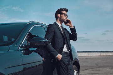 Always available. Handsome young businessman talking on the phone while standing near his car outdoors