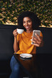 © StratfordProductions - An attractive smiling young woman taking selfie on mobile phone in cafe