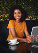 © StratfordProductions - Happy young woman with digital tablet and coffee cup in cafe