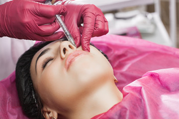 Cosmetologist making procedure. Dermatologist making an injection of botox or hyaluronic acid. Close up still of lip injection. Lip booster procedure. Beauty salon service.