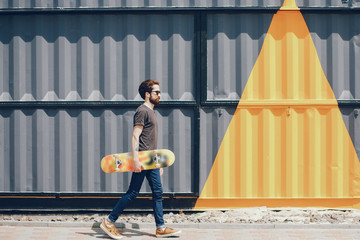 Handsome guy with a tattoo. A man standing near wall. The guy with a skateboard