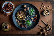 Healthy Teatime Oriental Style With Mint Tea, Dates, Walnuts And Pistachios  On Black Ornamental Tray Over Wooden Background