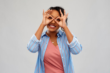 Sticker - people, gesture and portrait concept - happy african american young woman looking through finger glasses over grey background