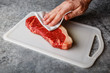 © The Picture Pantry - Raw fresh meat Steak Striploin on cutting board drying up excess moisture by Male hand with paper towel