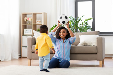 Wall Mural - childhood, kids and people concept - happy african american mother and her baby son playing with soccer ball together on sofa at home