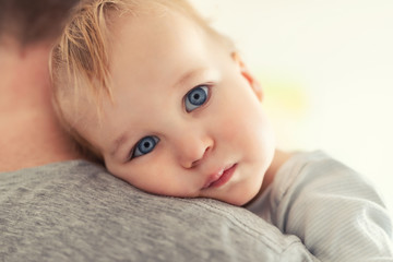 Close-up portrait of cute adorable blond caucasian toddler boy on fathers shoulder indoors. Sweet little child feeling safety on daddys hand. Responsibility and childcare. happy childhood