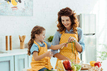 Wall Mural - cute daughter in polka dot yellow apron giving mother green onions