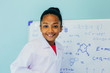 © twinsterphoto - African American girl in lab coat drawing mathematic and science formulas on white board. Creativity and Education concept