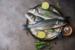 Flat lay fresh raw fish seabass in a plate with ice cubes, rosemary and lime on a dark rustic background. Top view, copy space.