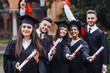 She is in a black mortar board, with red tassel, in gown, with nice brown curly hair, diploma in hand