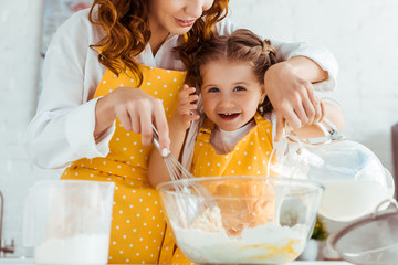 mother and excited daughter in aprons cooking dough in kitchen
