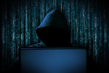 hacker with red glowing mask behind notebook laptop in front of blue source binary code background internet cyber hack attack concept