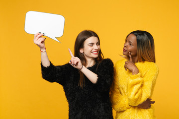 Two young women friends european and african american in black yellow clothes hold say clouds isolated on bright orange wall background, studio portrait. People lifestyle concept. Mock up copy space.