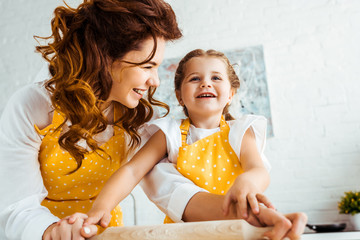 happy mother with excited daughter holding wooden rolling pin together