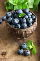 Wall Mural - Freshly picked blueberries in wooden bowl. Juicy and fresh blueberries with mint on wooden table. Bilberry on rustic background. Blueberry antioxidant. Concept for healthy eating and nutrition. 