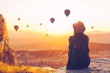 A Woman Alone Unplugged Sits On Top Of A Mountain And Admires The Flight Of Hot Air Balloons In Cappadocia In Turkey. Digital Detox And Soul Search