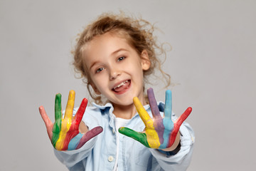 Beautiful little girl with a painted hands is posing on a gray background.