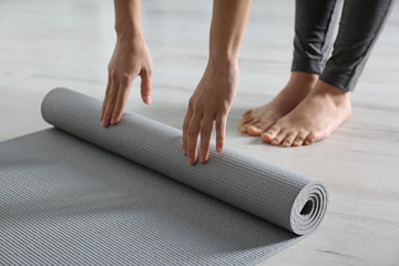 Woman rolling yoga mat on floor indoors, closeup