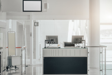 Wall Mural - An empty gate of a modern airport terminal with computer monitors on the counter desk, information screen on the top, baggage gauge, and the bright corridor leading to the airplane to boarding behind