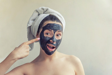 Wall Mural - Beauty portrait of woman in towel on head applying black nourishing mask on face, white background isolated. Skincare cleansing eco organic cosmetic spa relax concept