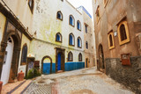 Fototapeta Uliczki - Narrow street of the old city with beige and white walls of the residential houses.