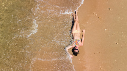 Aerial top view of young woman in bikini relaxing on sand tropical beach by sea and waves from above, girl on tropical island beach vacation in Thailand