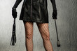 The dominant woman in a leather dress with a stack and a whip in her hand. Bdsm outfit