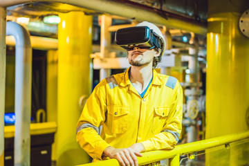 Young woman in a yellow work uniform, glasses and helmet uses virtual reality glasses in industrial environment, oil Platform or liquefied gas plant