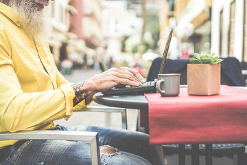 Trendy businessman using laptop in bar cafeteria outdoor - Mature hipster male browsing online and drinking coffee - Technology and fashion lifestyle concept - Focus on guy's hand