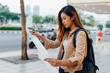 © twinsterphoto - Pretty casual Asian woman with backpack reading paper map while exploring city of Bangkok, Thailand